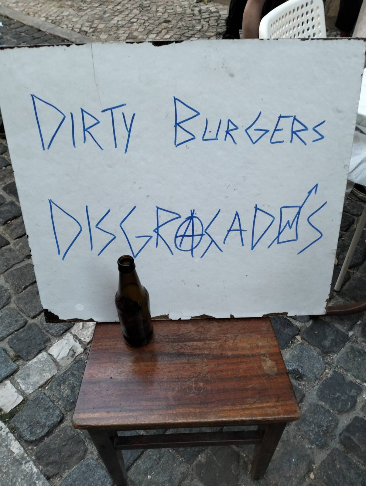 quadro branco com o texto “dirty burgers disgraçados” e uma garrafa de cerveja vazia à frente